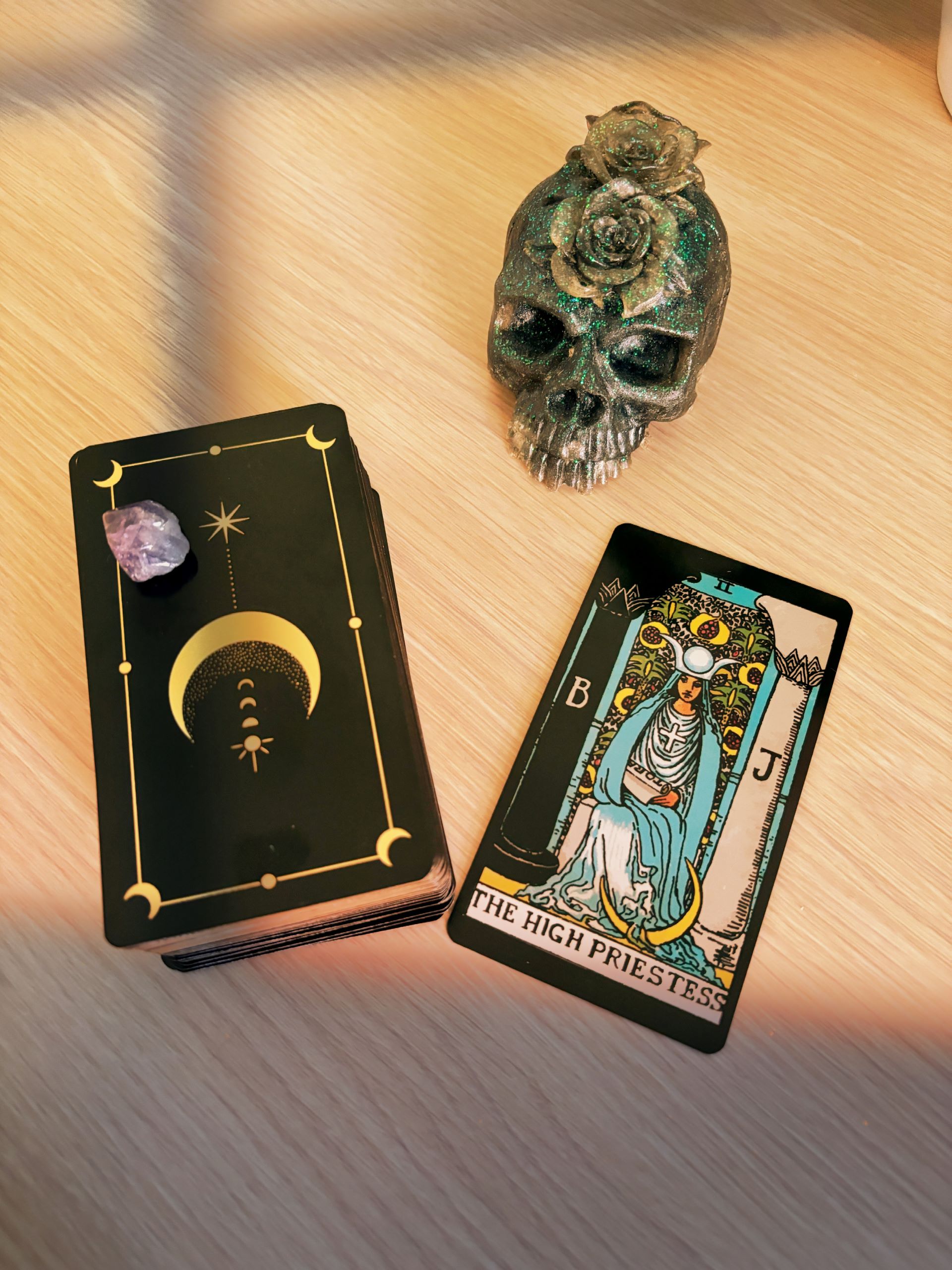 Tarot cards on a desk, The High Priestess card turned over, a skull with roses sits at the top