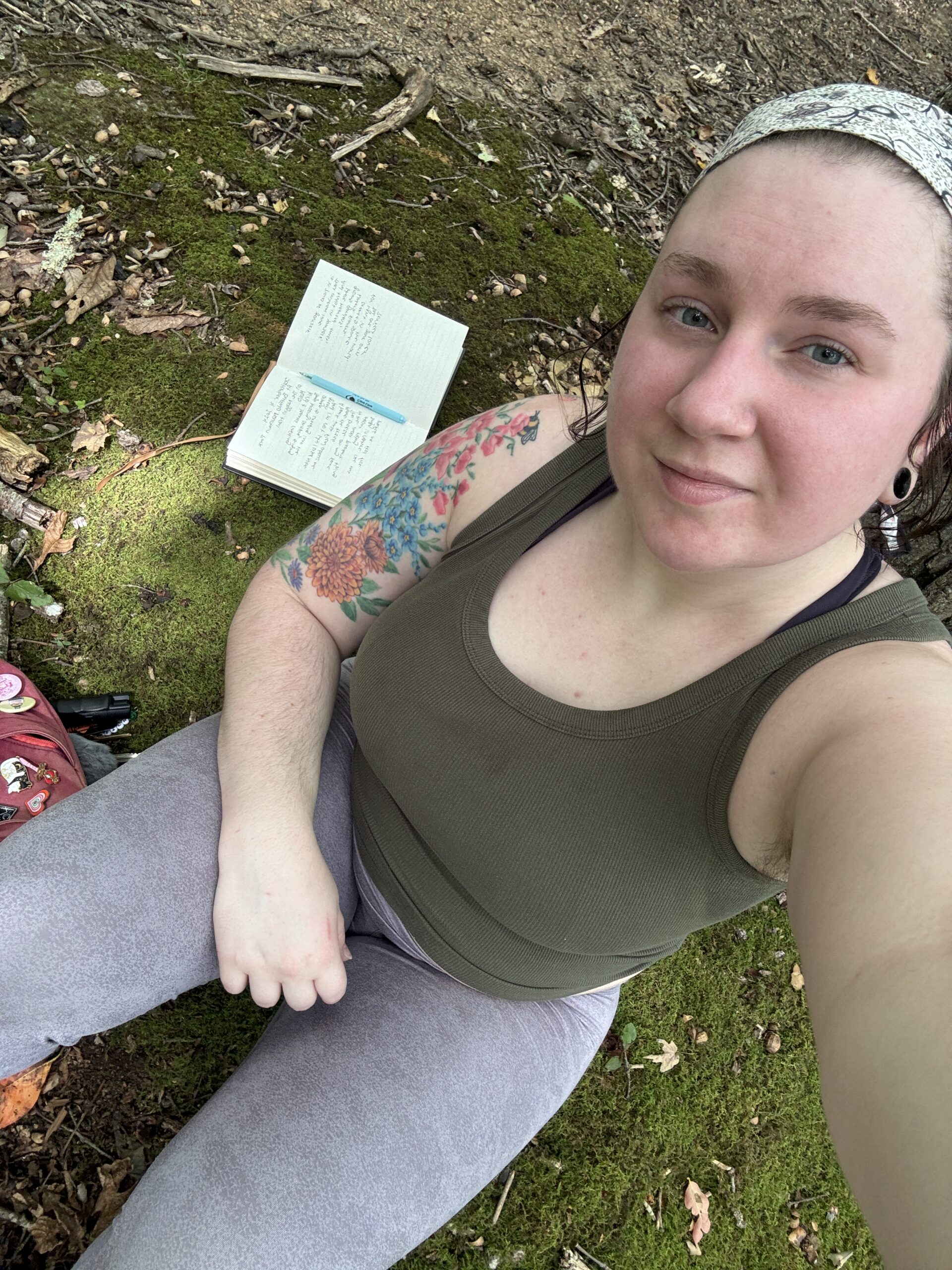 woman, kira sky, sitting on the mossy ground with a journal open next to her. 
